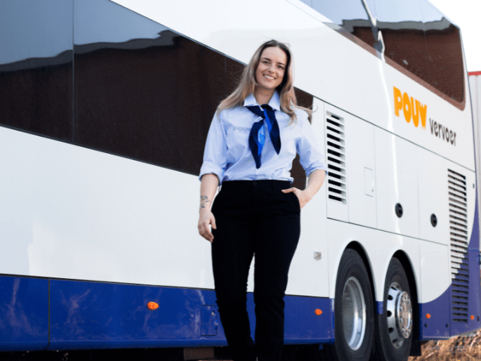 Vriendelijke vrouwelijke chauffeur van Pouw Vervoer poseert in uniform voor een moderne touringcar, klaar voor vertrek met passagiers